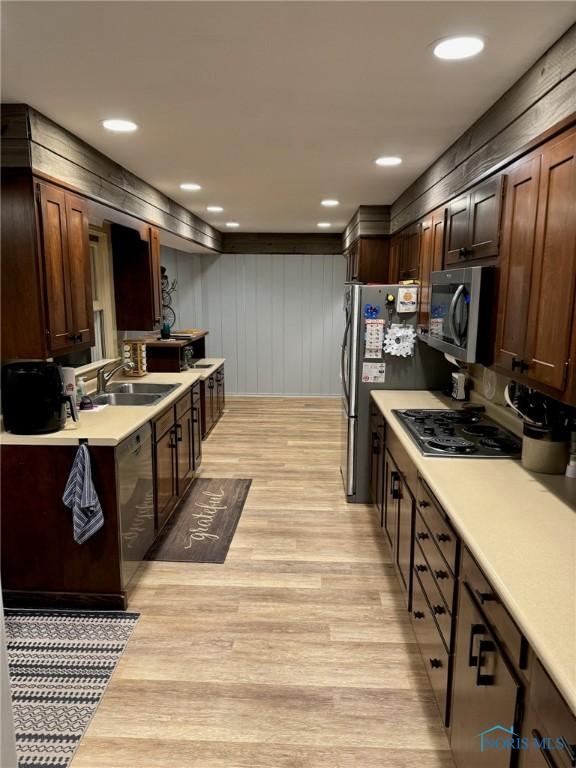 kitchen with dark brown cabinetry, sink, light hardwood / wood-style flooring, and appliances with stainless steel finishes