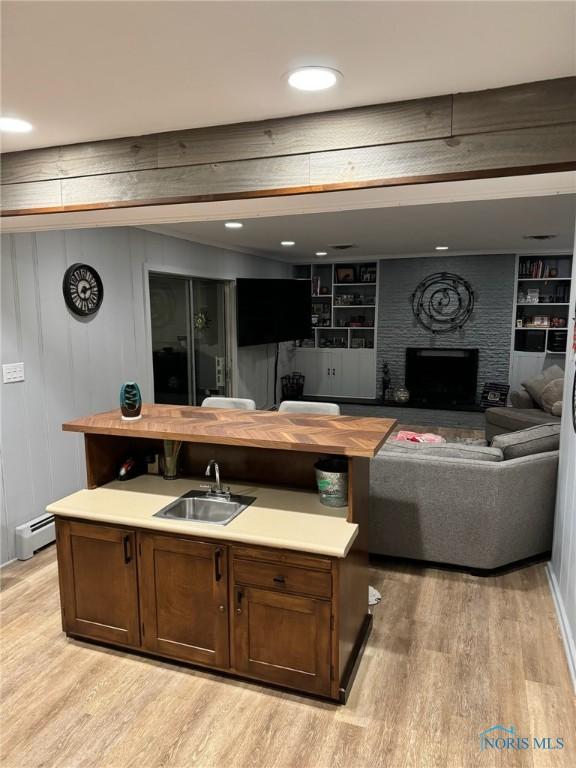 living room featuring sink, built in features, a baseboard heating unit, a brick fireplace, and light wood-type flooring