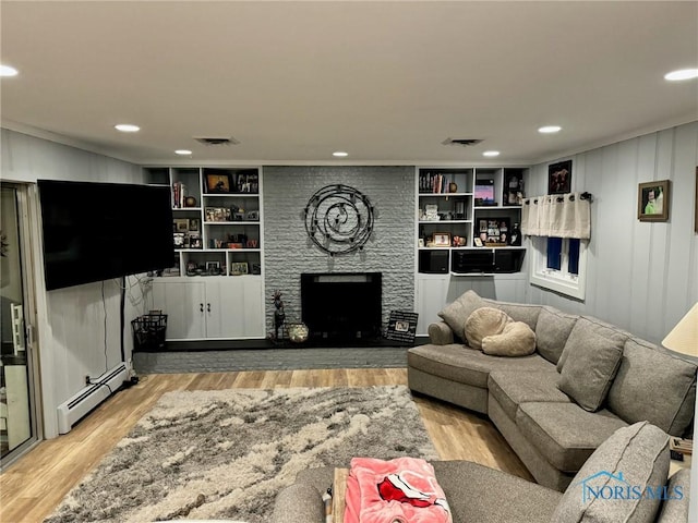 living room featuring built in shelves, a baseboard radiator, light hardwood / wood-style floors, and a large fireplace