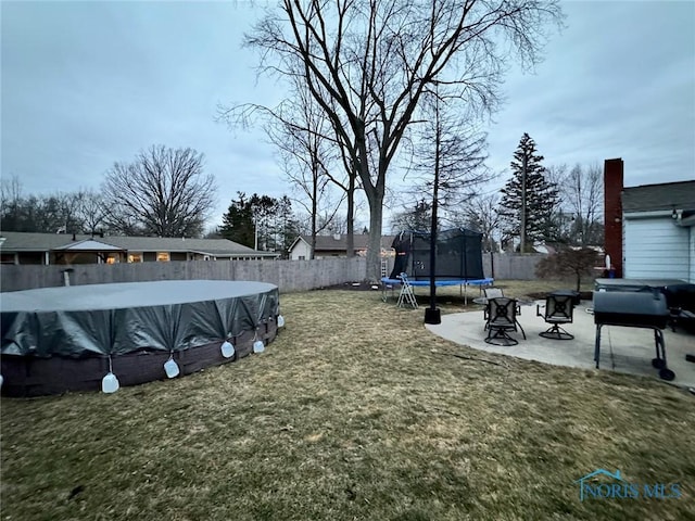 view of yard featuring a trampoline, a patio area, and a covered pool