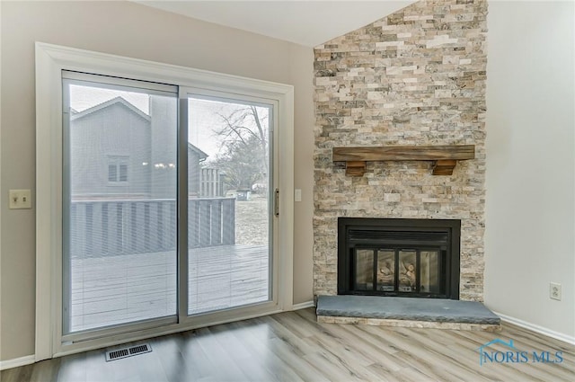 doorway featuring vaulted ceiling, a stone fireplace, and light hardwood / wood-style floors