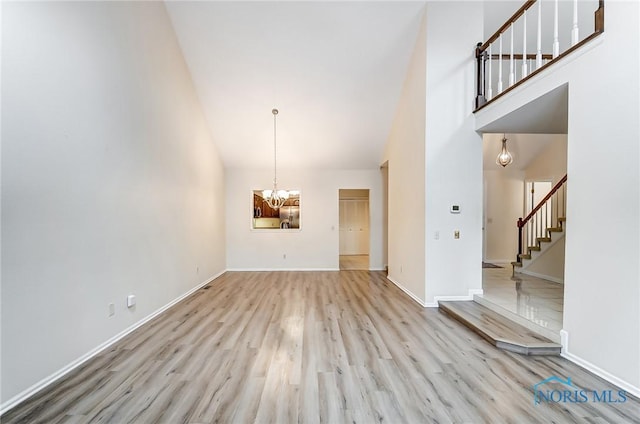 32 Abbey Rd, Perrysburg, OH 43551 - unfurnished living room with light wood-style flooring, high vaulted ceiling, an inviting chandelier, and stairway