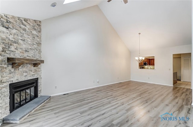 unfurnished living room with light hardwood / wood-style flooring, ceiling fan with notable chandelier, a fireplace, and high vaulted ceiling