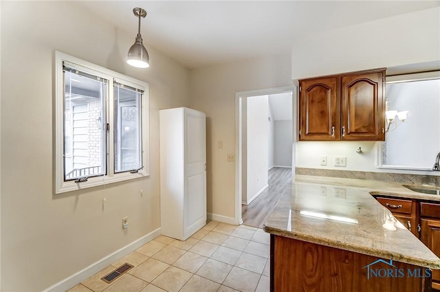 kitchen with hanging light fixtures, sink, light tile patterned floors, and light stone counters