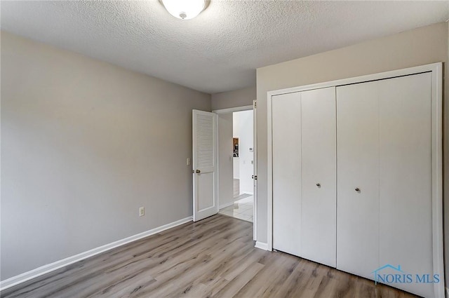 unfurnished bedroom featuring a textured ceiling, a closet, and light wood-type flooring