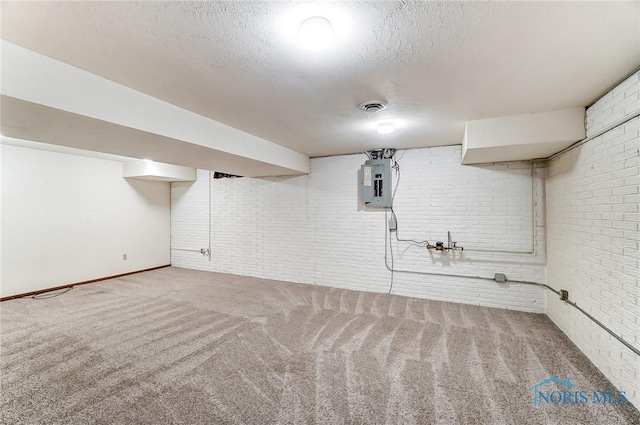 basement featuring brick wall, carpet, electric panel, and a textured ceiling