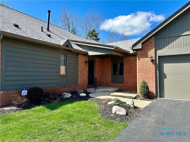32 Abbey Rd, Perrysburg, OH 43551 - view of exterior entry with driveway, an attached garage, brick siding, a yard, and a shingled roof