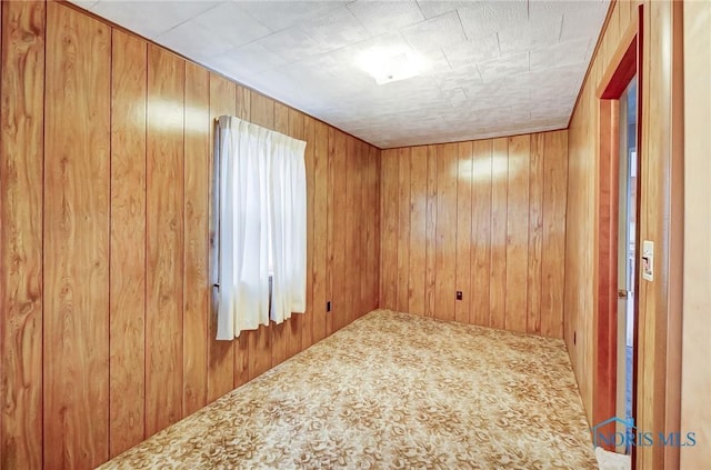 carpeted spare room featuring wood walls