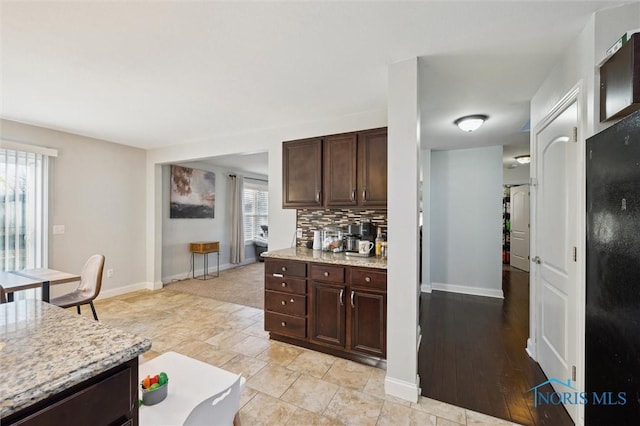 kitchen featuring decorative backsplash, light stone countertops, and dark brown cabinets