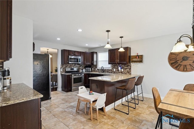 kitchen featuring stainless steel appliances, decorative backsplash, light stone counters, and decorative light fixtures