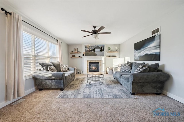 living room featuring a fireplace, ceiling fan, and carpet