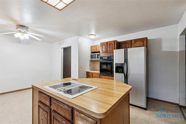 kitchen with appliances with stainless steel finishes, a center island, light tile patterned floors, and ceiling fan