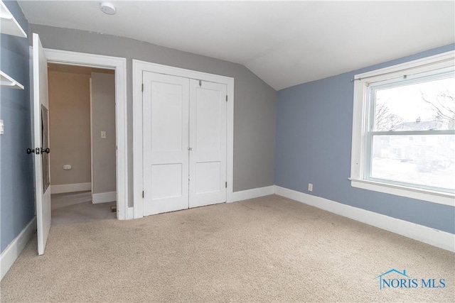 unfurnished bedroom with a closet, lofted ceiling, and light carpet