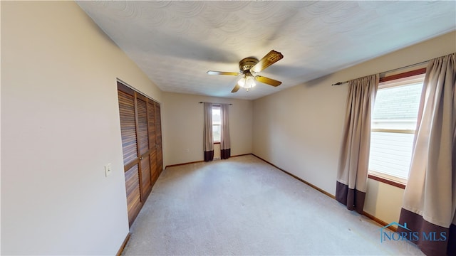 unfurnished bedroom featuring ceiling fan, a closet, light colored carpet, and multiple windows