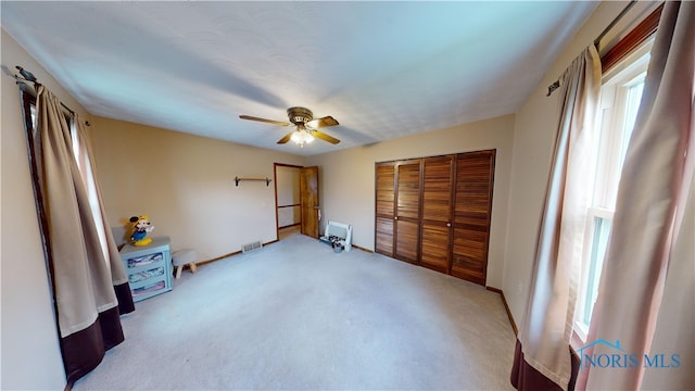 unfurnished bedroom featuring ceiling fan, multiple windows, a closet, and light carpet