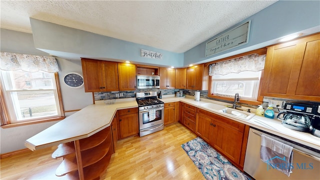 kitchen with appliances with stainless steel finishes, sink, decorative backsplash, a textured ceiling, and light hardwood / wood-style flooring