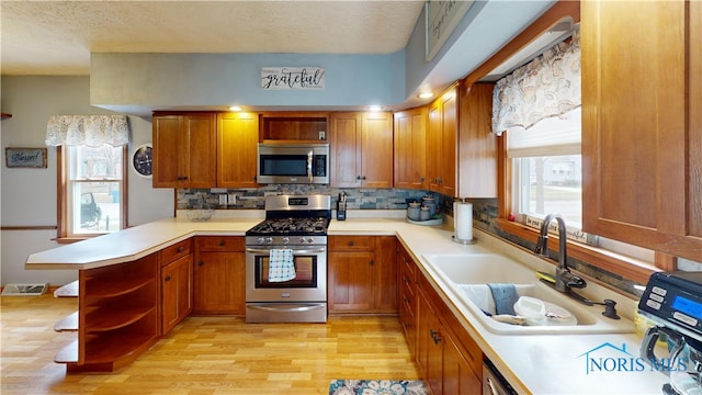 kitchen featuring appliances with stainless steel finishes, sink, kitchen peninsula, a textured ceiling, and light hardwood / wood-style flooring