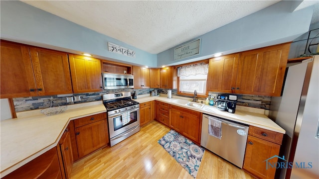 kitchen featuring sink, light hardwood / wood-style flooring, stainless steel appliances, a textured ceiling, and decorative backsplash