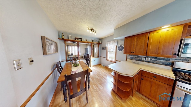 kitchen featuring tasteful backsplash, stove, kitchen peninsula, a textured ceiling, and light hardwood / wood-style flooring