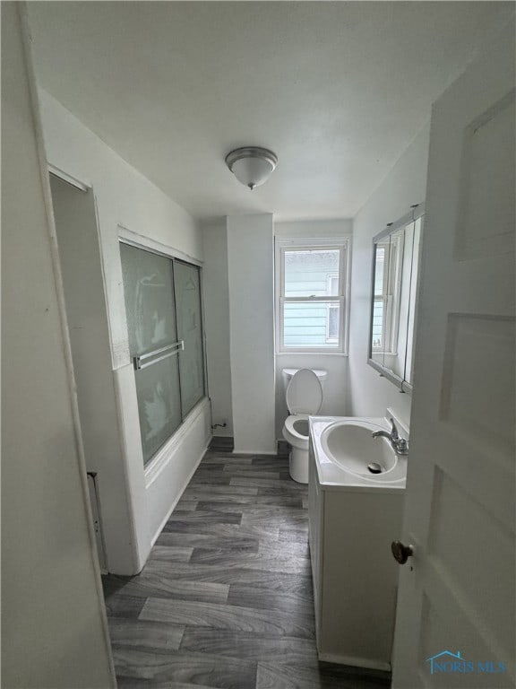 full bathroom with vanity, hardwood / wood-style floors, shower / bath combination with glass door, and toilet