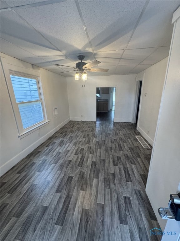 unfurnished living room with a drop ceiling, dark hardwood / wood-style flooring, and ceiling fan