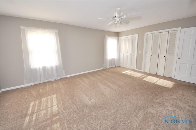 unfurnished bedroom with ceiling fan, carpet floors, multiple windows, and two closets