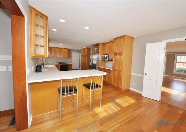 kitchen featuring sink, a breakfast bar, appliances with stainless steel finishes, light hardwood / wood-style floors, and kitchen peninsula