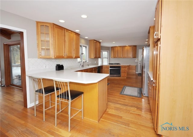 kitchen featuring a breakfast bar, appliances with stainless steel finishes, backsplash, kitchen peninsula, and light wood-type flooring