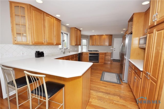 kitchen featuring sink, light hardwood / wood-style flooring, a kitchen breakfast bar, stainless steel appliances, and kitchen peninsula