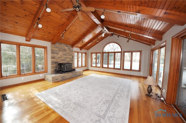 unfurnished living room featuring lofted ceiling with beams, wooden ceiling, a wood stove, track lighting, and light hardwood / wood-style floors