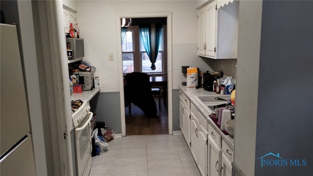 kitchen featuring white cabinetry, white gas range oven, and refrigerator