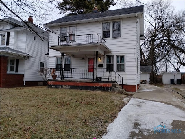 view of front property featuring an outbuilding, a balcony, a garage, and a front yard