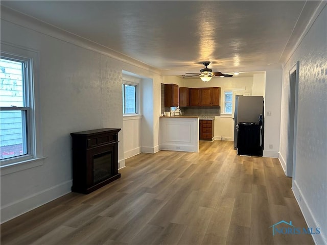 kitchen featuring light wood-style flooring, backsplash, a glass covered fireplace, and freestanding refrigerator