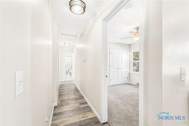 hall featuring dark carpet, attic access, and baseboards