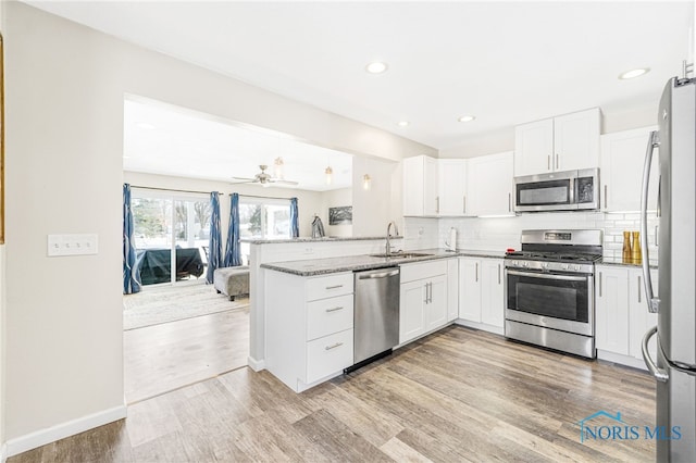 kitchen with stainless steel appliances, light wood-style floors, white cabinetry, a sink, and a peninsula