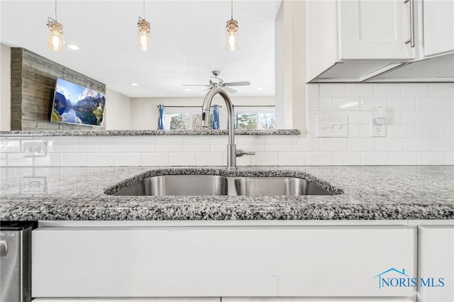 kitchen with decorative backsplash, white cabinets, light stone counters, hanging light fixtures, and a sink