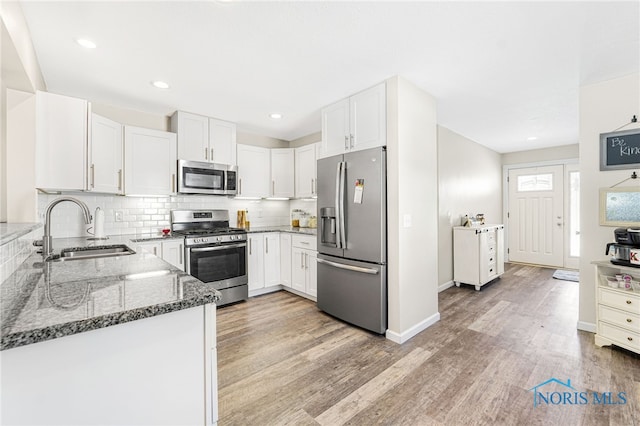 kitchen featuring a sink, white cabinets, appliances with stainless steel finishes, light wood finished floors, and dark stone countertops