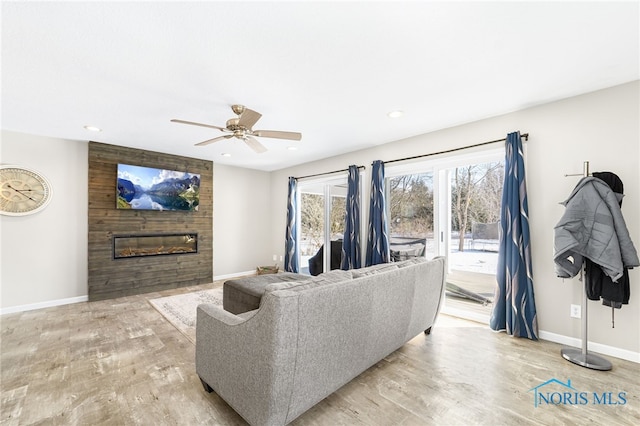 living room featuring a large fireplace, recessed lighting, baseboards, and light wood-style floors