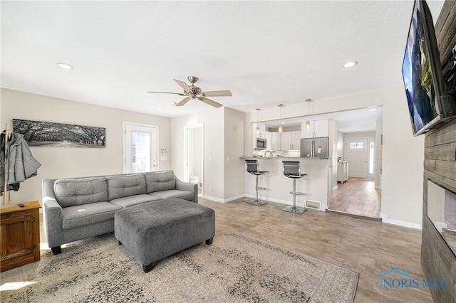 living room featuring visible vents, baseboards, light wood-style flooring, ceiling fan, and recessed lighting