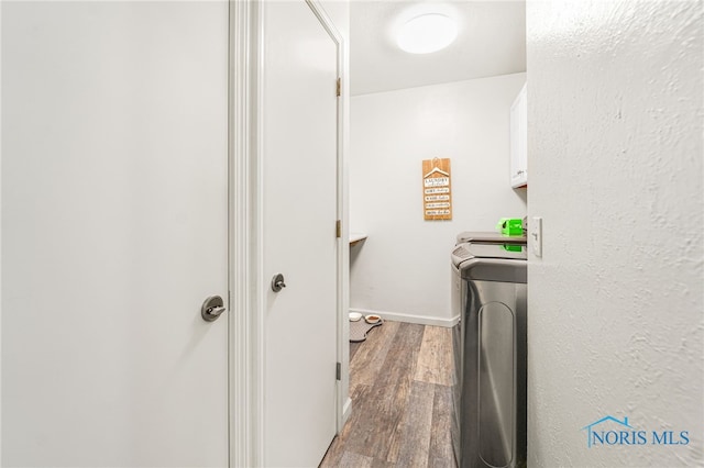 clothes washing area featuring wood finished floors, washing machine and clothes dryer, cabinet space, and baseboards