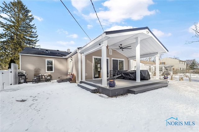 snow covered rear of property with ceiling fan and fence