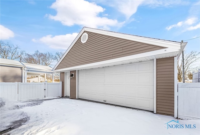 snow covered garage with a garage and fence