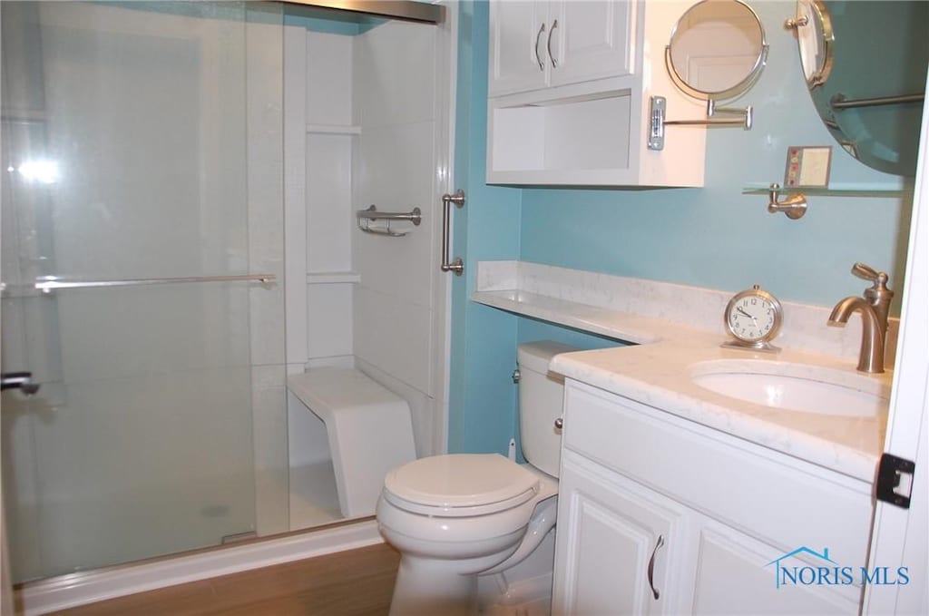 bathroom featuring vanity, hardwood / wood-style flooring, a shower with shower door, and toilet