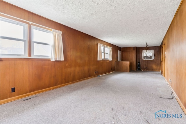 empty room featuring wooden walls, light colored carpet, and a textured ceiling