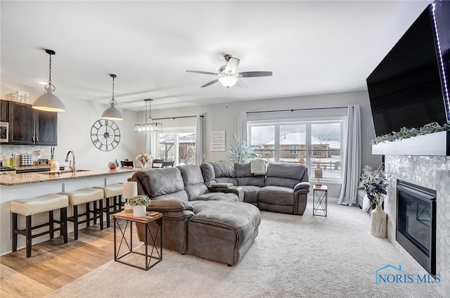 living room with ceiling fan, sink, a fireplace, and light wood-type flooring