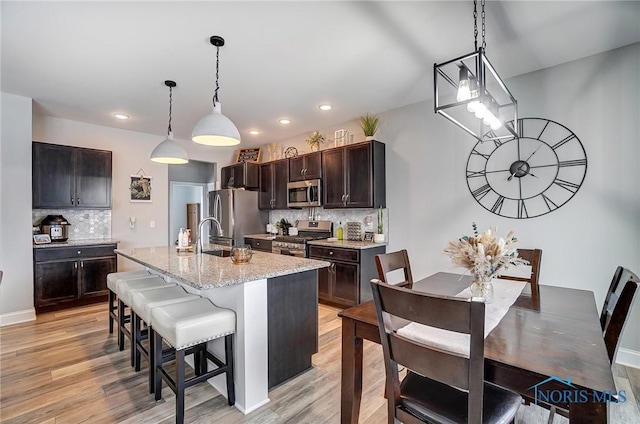 kitchen featuring stainless steel appliances, a breakfast bar, a center island with sink, and light hardwood / wood-style floors