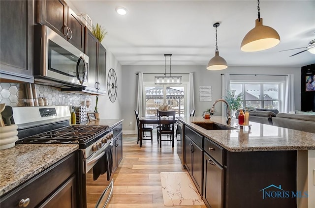 kitchen featuring sink, hanging light fixtures, a center island with sink, stainless steel appliances, and light stone countertops