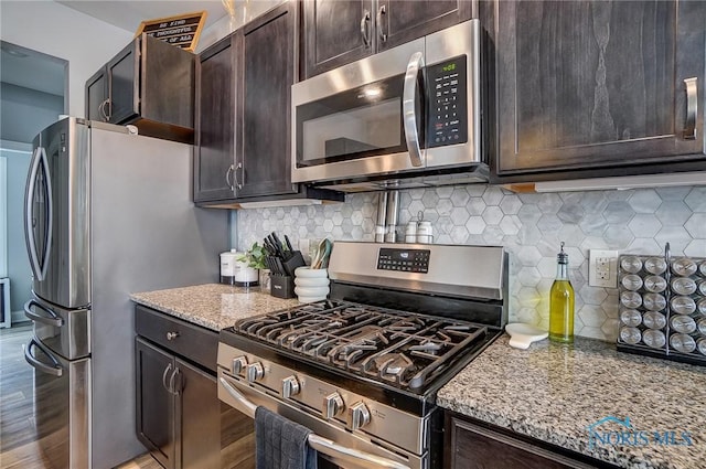 kitchen with appliances with stainless steel finishes, backsplash, light stone counters, dark brown cabinetry, and wood-type flooring