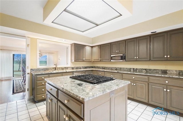 kitchen with a skylight, sink, a center island, light stone counters, and stainless steel appliances