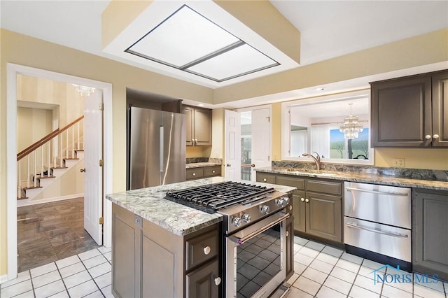 kitchen featuring sink, light tile patterned floors, appliances with stainless steel finishes, an inviting chandelier, and a center island